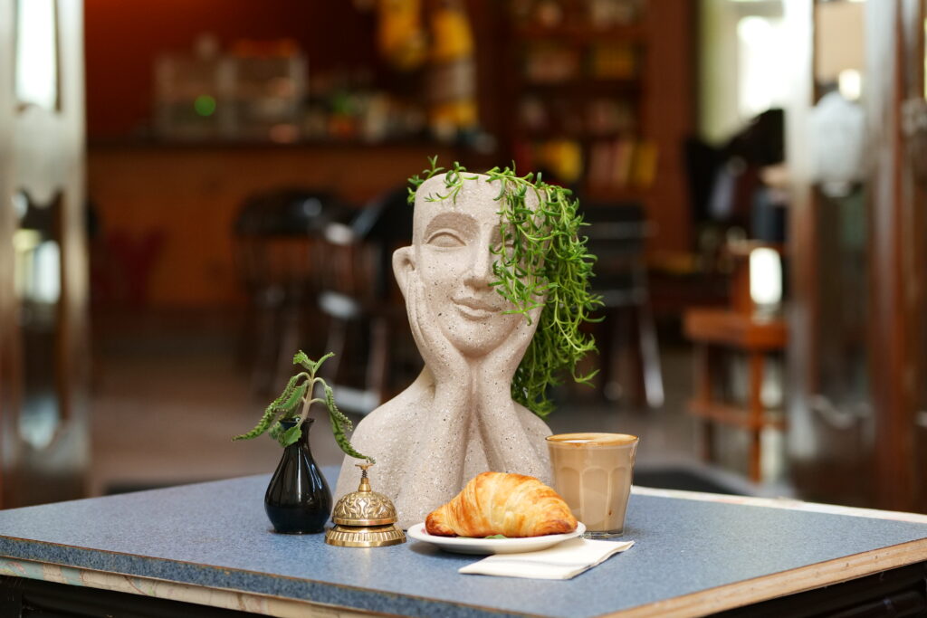 Croissant and Coffee with a small bell, a statue, and a plant